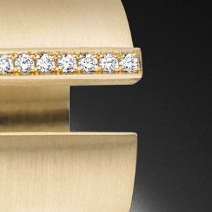 Breiter Goldring besetzt mit Diamanten vor einem schwarzen Hintergrund